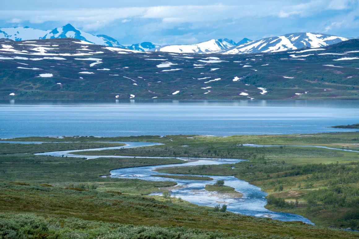Řeka LåddeJåhkå a jezero Vastenjaure, v pozadí vrcholky norských hor